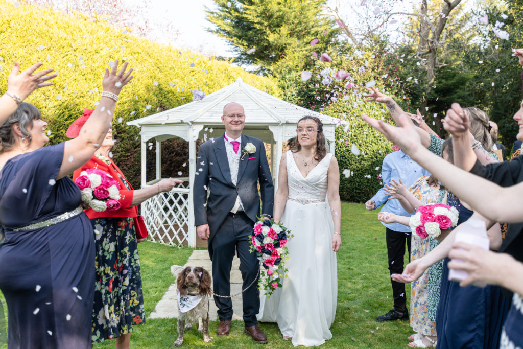Wedding guests throwing colourful confetti over Becky and Steve outside Charlecote Pheasant Hotel