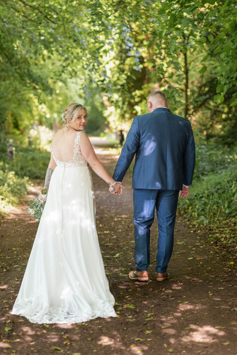​Newlyweds walking hand-in-hand through a sunlit garden, highlighting unposed and joyful wedding photography.