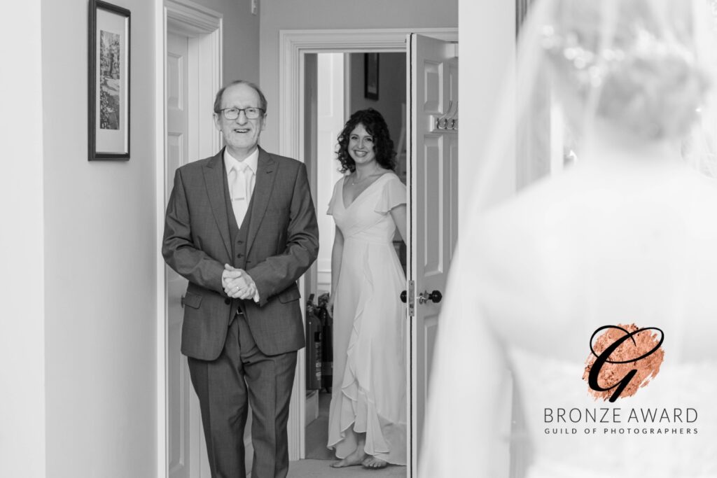 Emotional Wedding Moment::A bride and her father share a joyful moment before the ceremony, with an excited look on his face as he waits in the doorway.