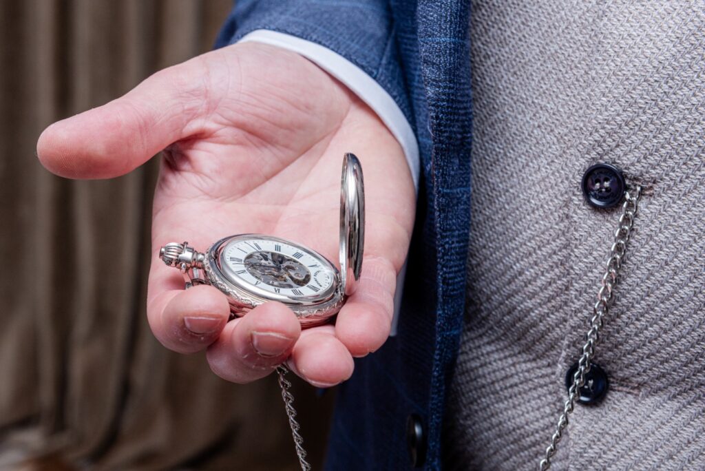 A close-up of a hand holding an antique pocket watch with an open face, revealing the intricate clockwork inside, set against a softly blurred background.