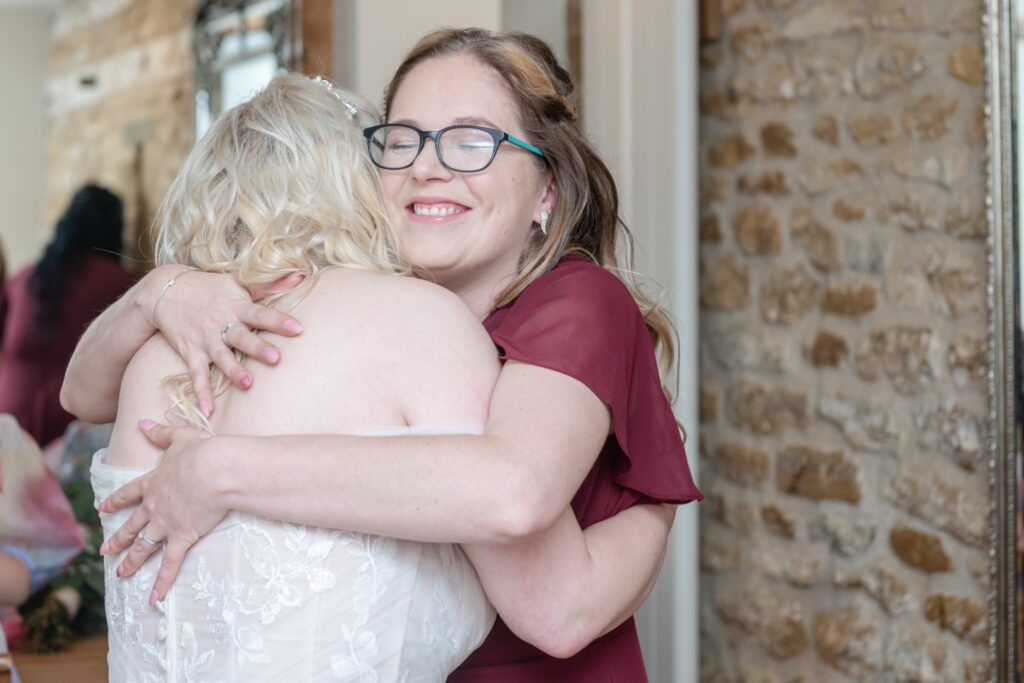 Two women share a heartfelt hug in a beautifully decorated room, capturing a moment of joy and friendship during a wedding celebration.
