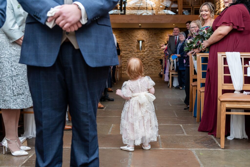 A young girl in a beautiful dress walks down the aisle at a wedding ceremony, with guests sitting on either side.