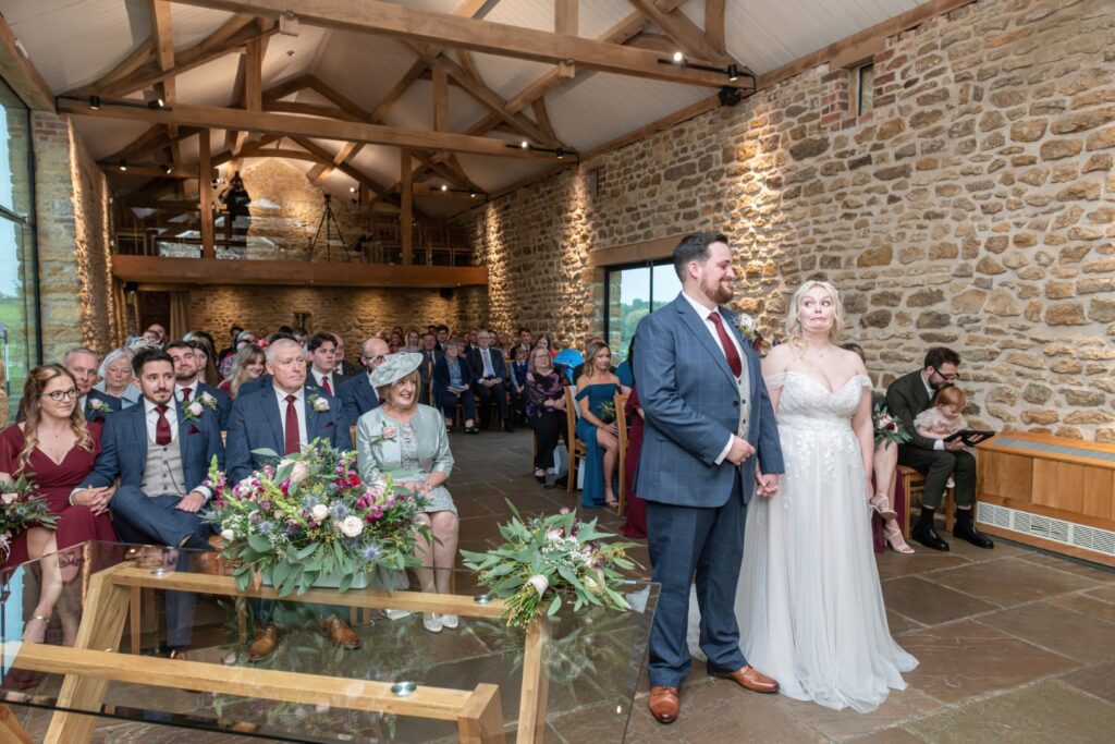 A couple stands hand in hand during their wedding ceremony, surrounded by family and friends in a beautifully decorated venue.