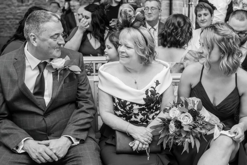 A couple seated at a wedding, sharing a light-hearted conversation while surrounded by smiling guests, capturing the essence of celebration and togetherness.