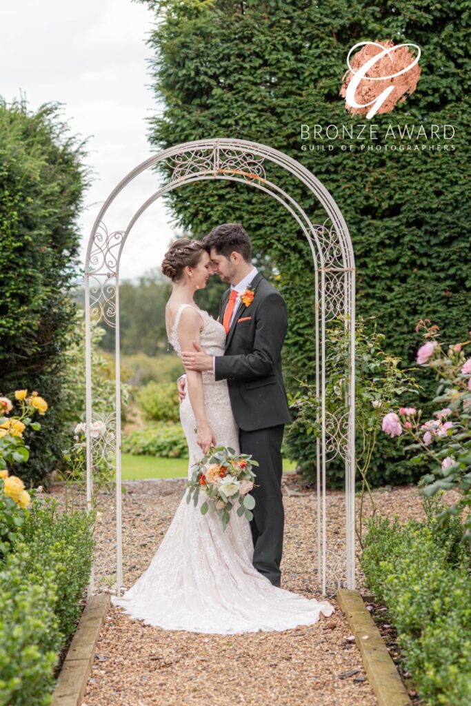 A couple sharing a tender moment under a beautifully designed arbor, surrounded by lush greenery and vibrant flowers.