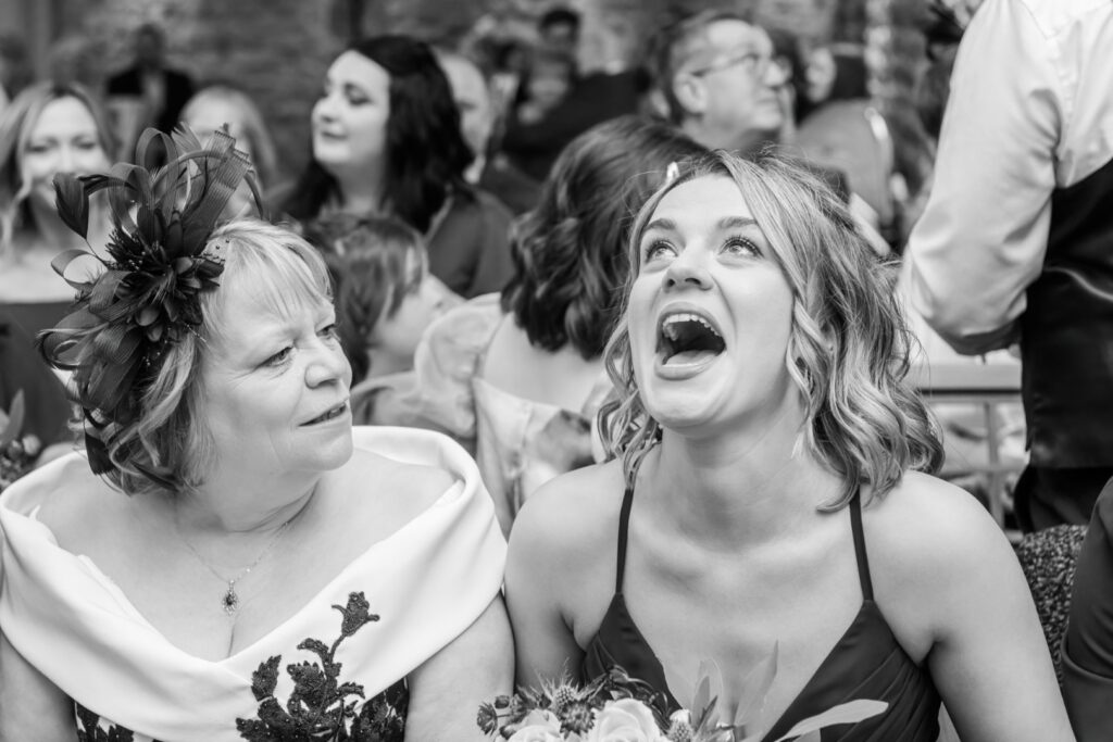 A candid black and white photograph capturing two women during a lively event, with one joyfully laughing and the other observing with a thoughtful expression.