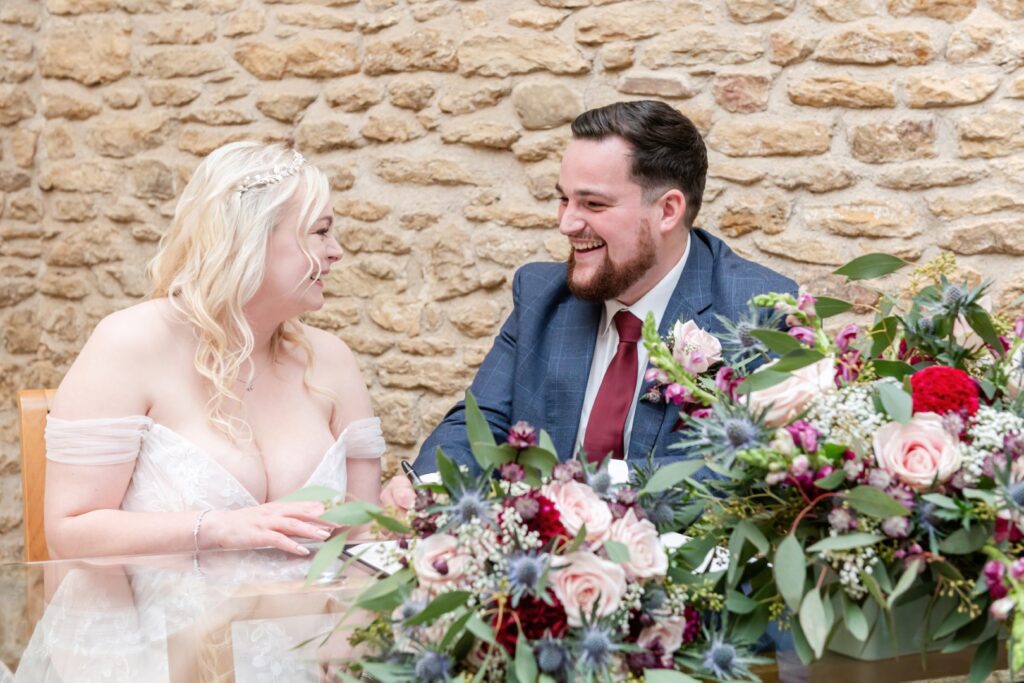 Couple joyfully signing their marriage document surrounded by beautiful floral arrangements.