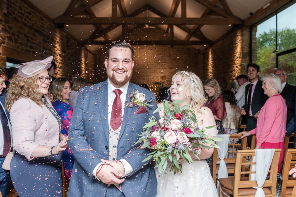A happy couple celebrates their wedding with confetti, surrounded by joyful guests in a beautiful venue.