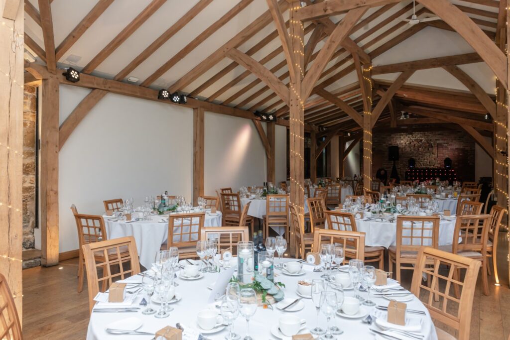A beautifully arranged dining area featuring wooden beams, tables with white linens, and elegant table settings, ready for a celebration.