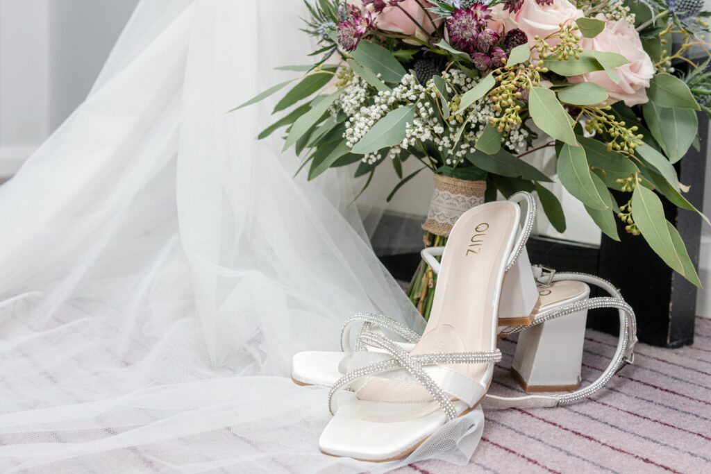 A pair of elegant bridal shoes beside a lush wedding bouquet on a soft surface.
