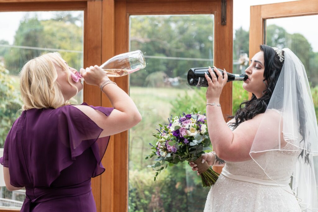 Two women toasting with champagne and wine inside a cozy venue, showcasing wedding festivities.