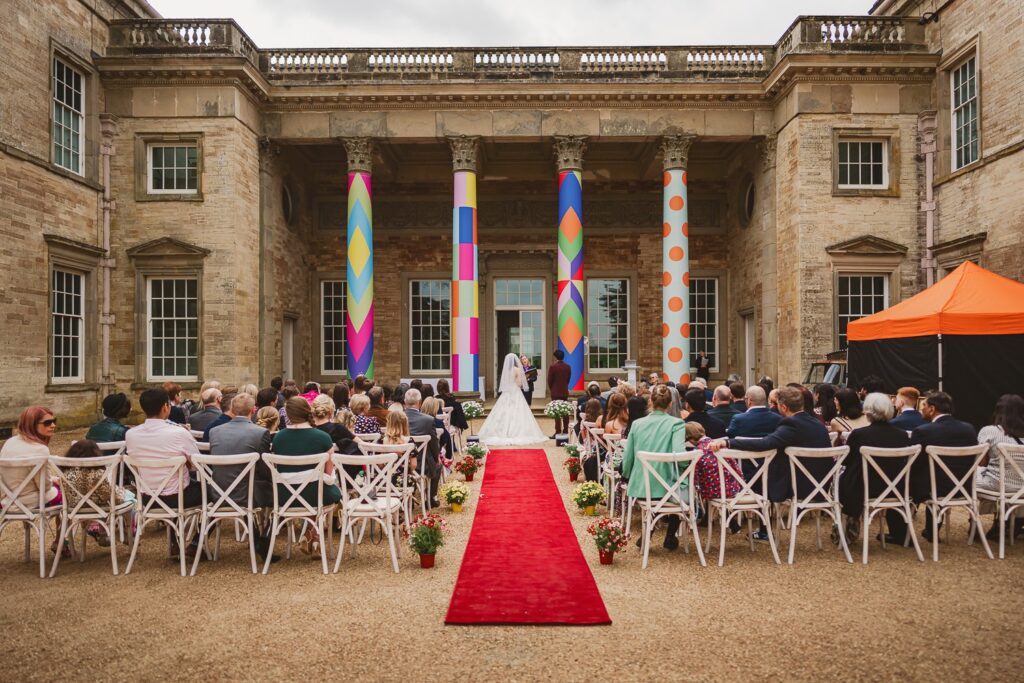 Outdoor wedding ceremony at Compton Verney with vibrant art pillars, combining modern style and historic architecture.