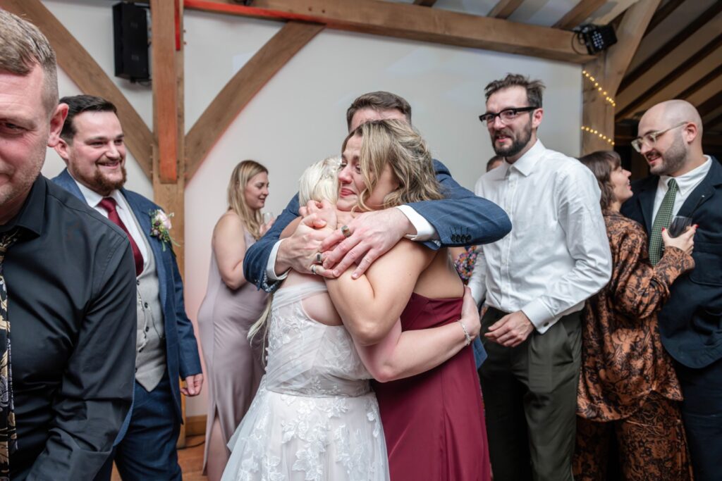 Two women sharing a heartfelt embrace amidst a joyful gathering, surrounded by friends and family in a decorated venue.