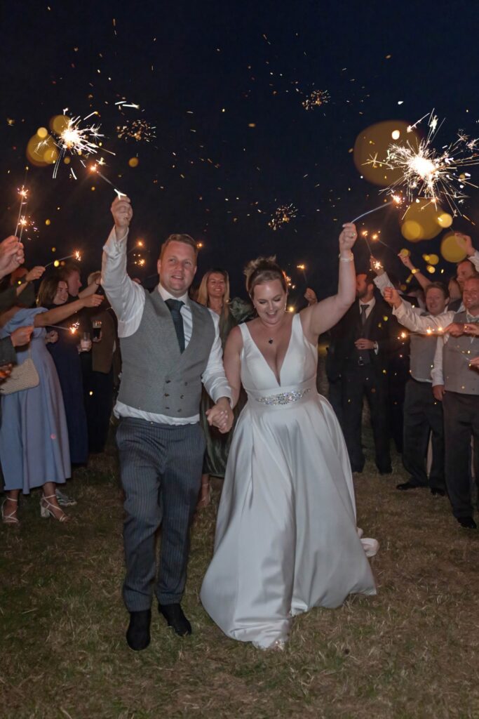 Newlyweds walking through a sparkler tunnel with guests cheering around them