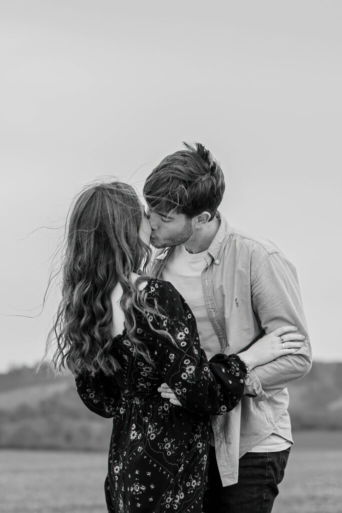 Couple sharing a kiss in a field, captured in black-and-white photography.
