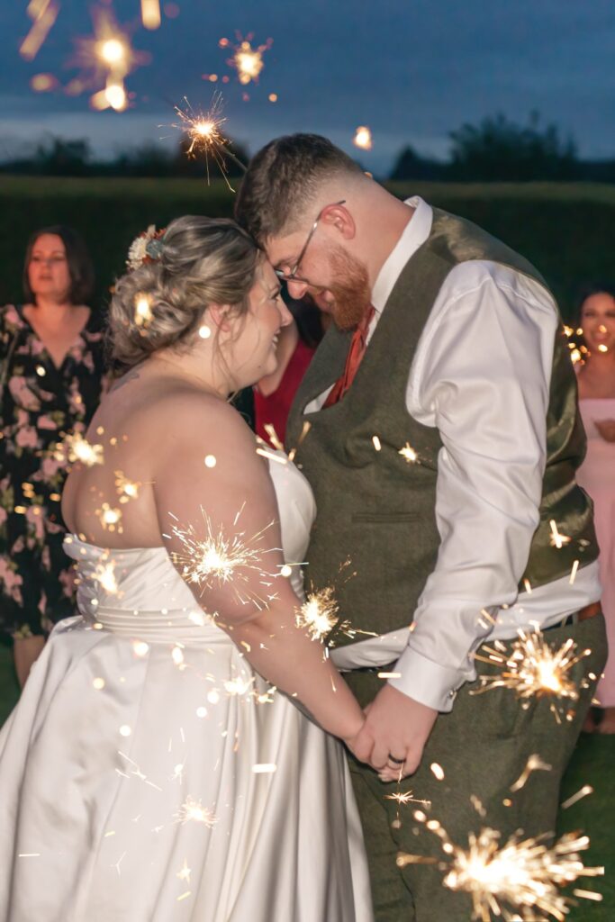 Romantic sparkler moment at twilight as couple lean their foreheads together
