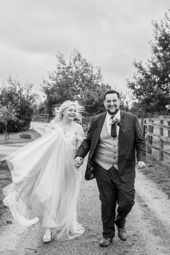 A happy bride and groom, hand in hand, walking down a scenic path surrounded by trees, dressed in formal wedding attire.