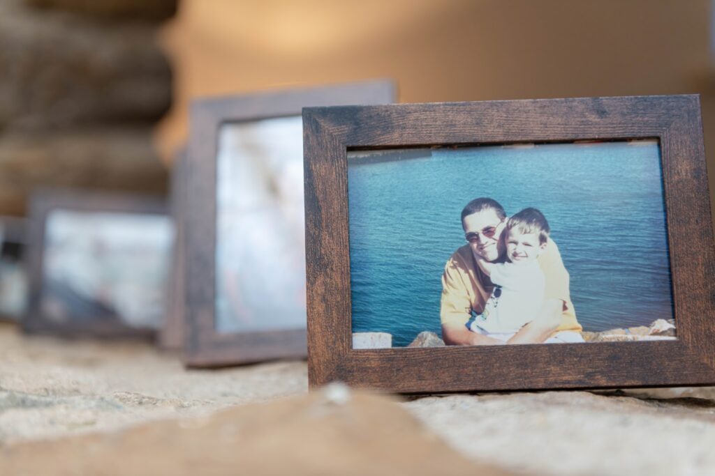 A close-up of a framed photo showing a man and a child smiling together by the water, with other blurred frames in the background.