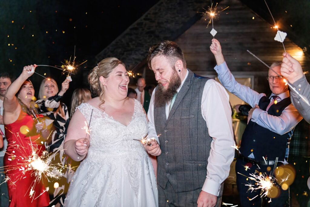 Bride and groom celebrating with sparklers surrounded by friends and family