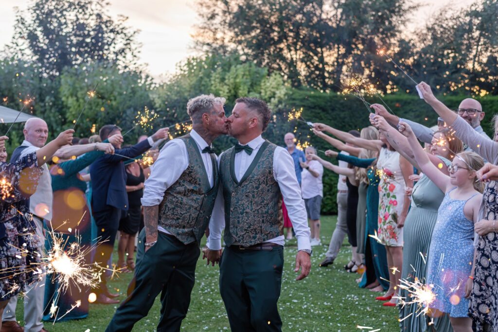 Same-sex couple kiss during sparkler tunnel moment at blue hour