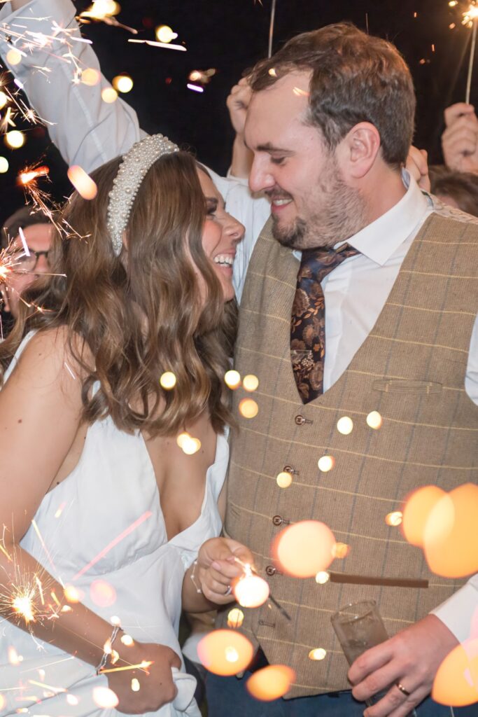 Couple laughing during sparkler wedding photos surrounded by glowing lights