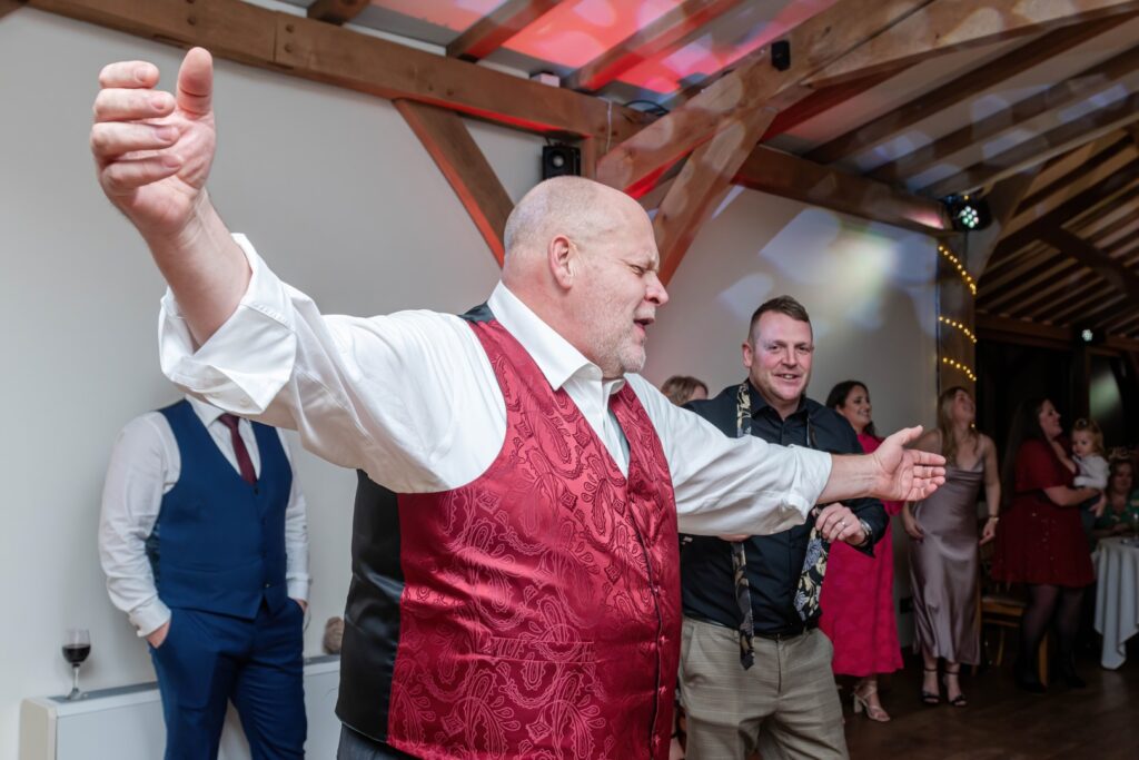 A man in a red vest embraces the dance floor, surrounded by an enthusiastic crowd during a festive event.