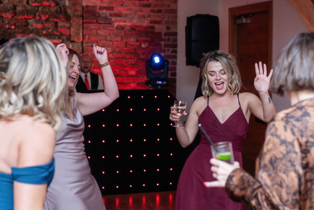 Group of women dancing and enjoying drinks at a lively event with a DJ in the background.