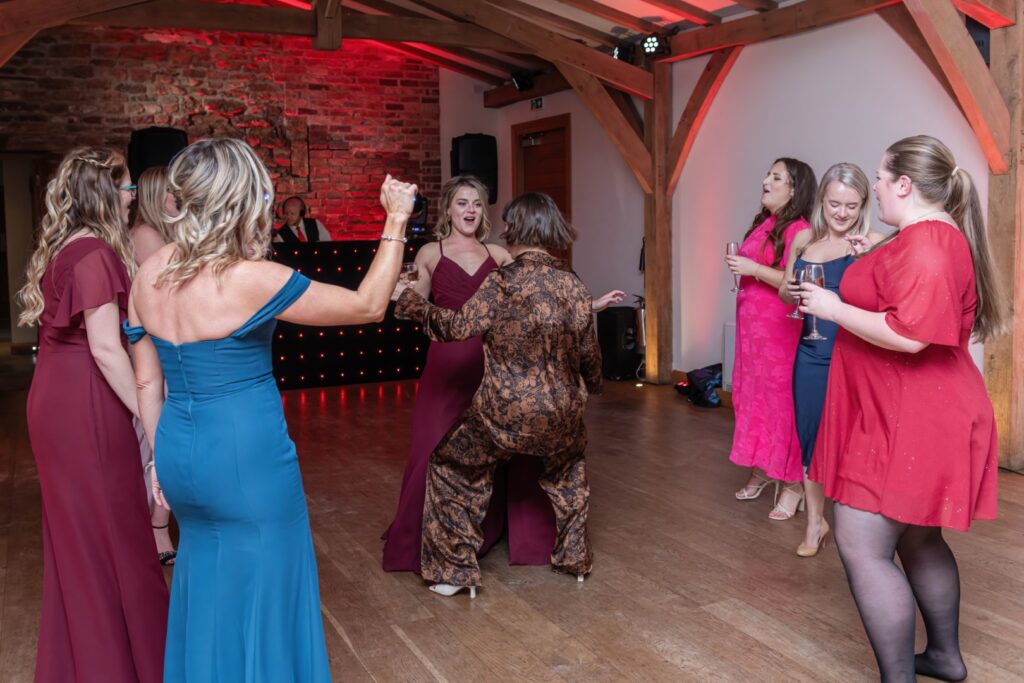 A lively gathering of women dancing and enjoying drinks at a festive event, with colorful outfits and a DJ in the background.
