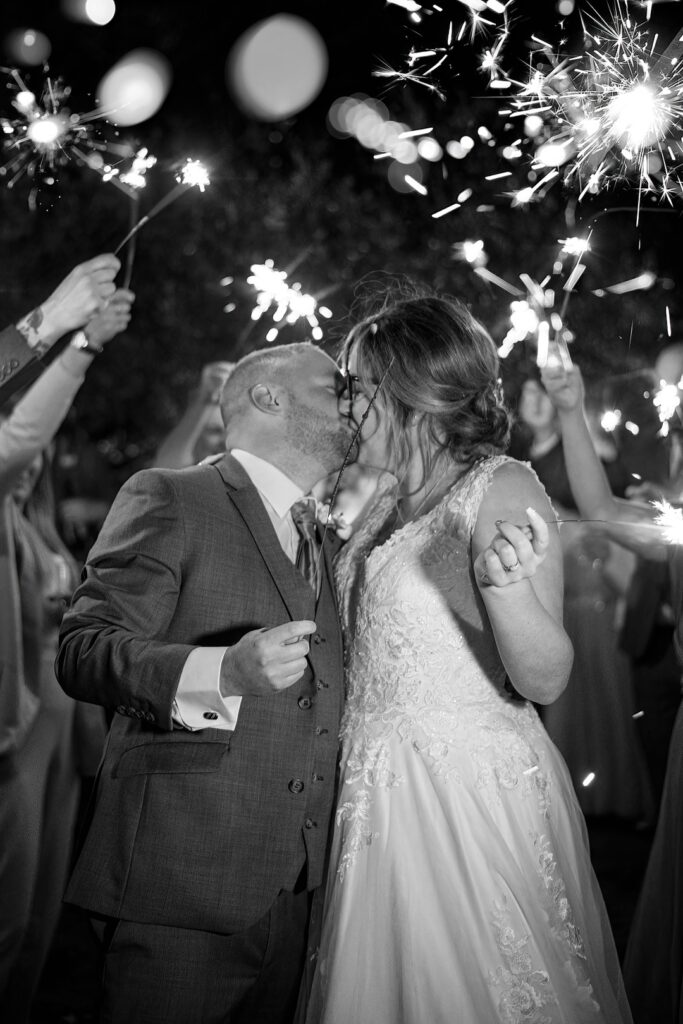 Black and white sparkler wedding photo of bride and groom sharing a kiss