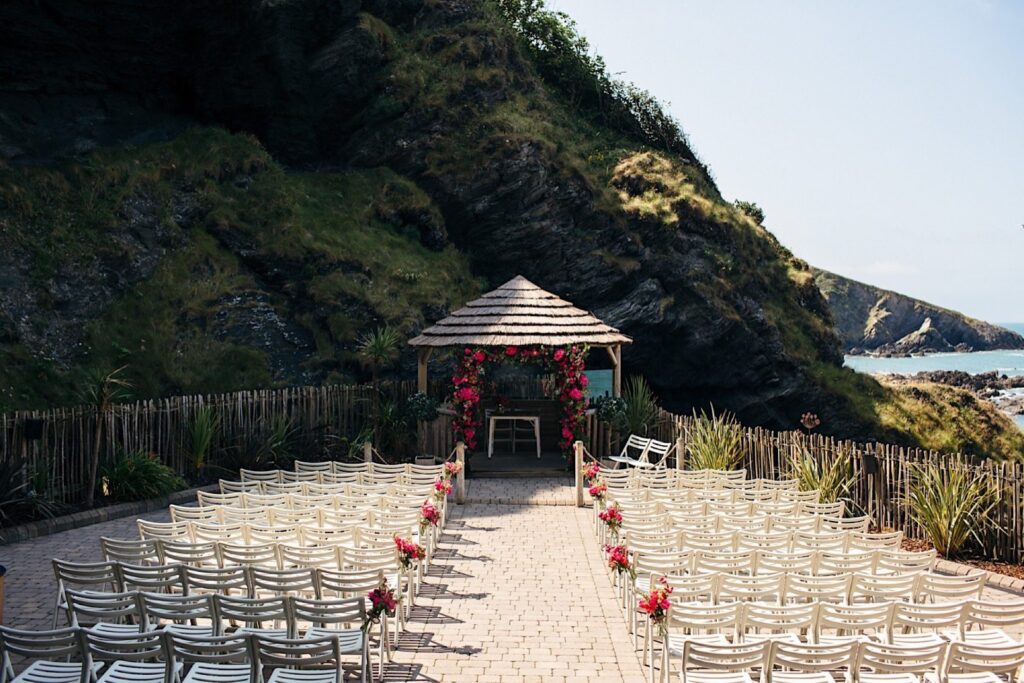 Seaside wedding ceremony setup with rows of white chairs facing a gazebo at Tunnels Beaches, a coastal venue in Devon.