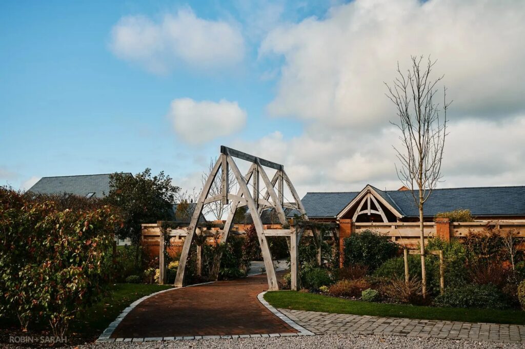 Rustic wedding barn exterior at Cider Mill Barns, featuring landscaped gardens and oak beams under a blue sky.