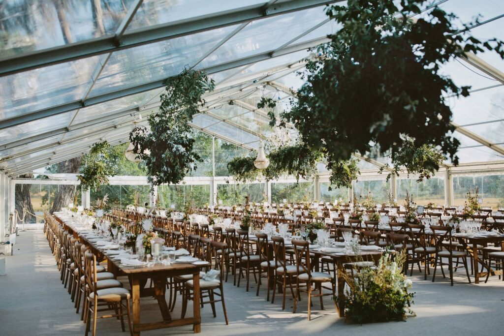 Long banquet-style wedding reception under a clear marquee at Wilderness Reserve, with hanging greenery and countryside views.