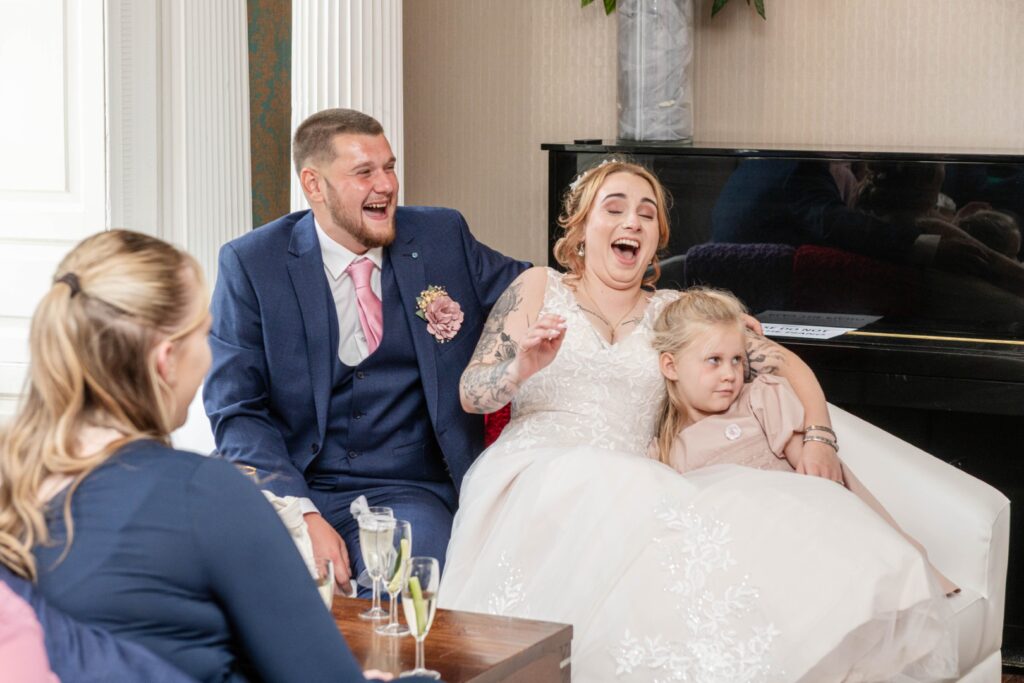 A couple shares a lighthearted moment with laughter while a young girl observes, all set in an elegant venue.