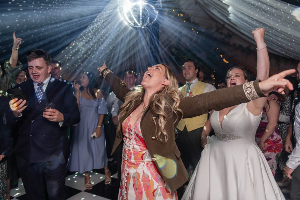 An energetic crowd enjoying a lively dance party with a disco ball overhead and vibrant lights illuminating the scene.