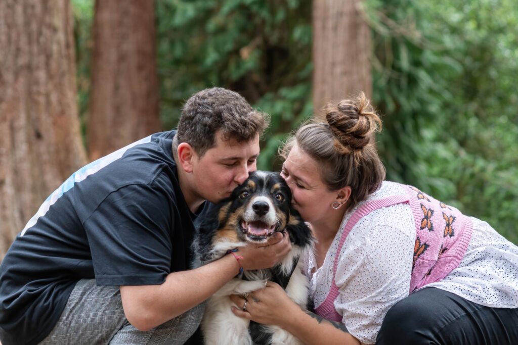 Laid-back woodland engagement session with couple kissing their dog – real, unposed moment from couples portfolio